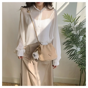 Detail of apricot drawstring bucket bag with metal chain strap and white plush charm