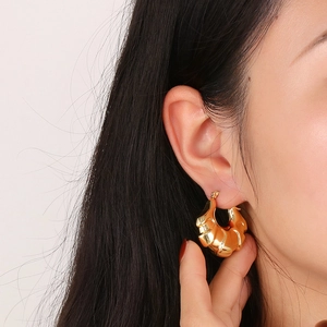 Detail of 18k gold plated hollow hoop earrings with textured croissant pattern on model