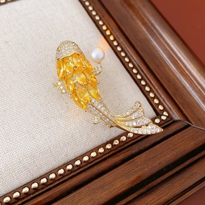 Detail of a golden carp brooch with yellow crystals and a white pearl on fabric