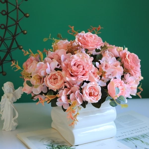 Pink silk roses and peonies in a white square ceramic pot against a dark green wall