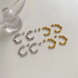 Irregular wavy C-shape gold and silver stud earrings set on a textured surface