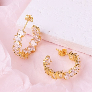 Close-up of gold-plated C-shaped earrings with white zircon on pink textured background
