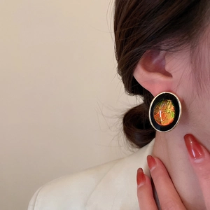 Close-up of vintage geometric round earring with gold trim and orange resin on model