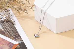 Silver heart pendant necklace hanging on a white geometric block with dried flowers