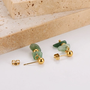 Detail of gold stud earrings with irregular green natural stones on beige textured rock
