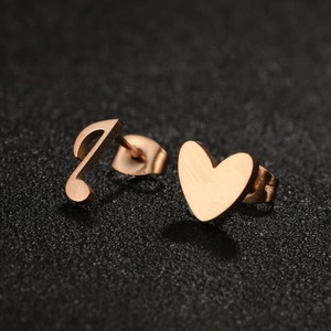 Rose gold asymmetrical heart and musical note stud earrings on a textured black surface
