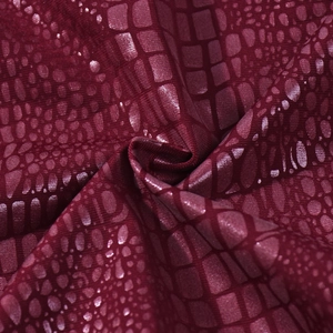 Macro detail of wine red faux crocodile skin fabric with metallic finish and texture