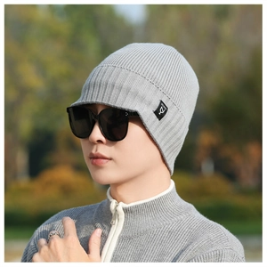 Detail of grey knitted beanie with logo tag worn by male model in winter outdoor setting