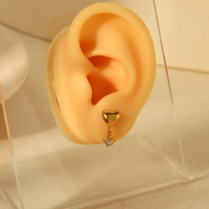 Detailed close-up of golden heart earrings with a clear zircon pendant on a display stand
