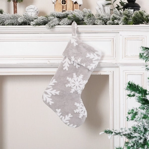 Gray plush Christmas stocking with white snowflake patterns hanging on a fireplace