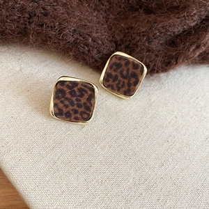 Détail de boucles d'oreilles carrées léopard avec bord doré sur toile beige neutre