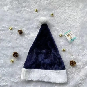 Flat lay detail of a navy blue plush Santa hat with a white pompom and pinecone decor