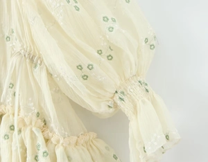 Dettaglio dei polsini elastici e ricami floreali verdi su un abito color bianco panna