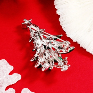 Silver Christmas tree brooch with green accents on festive red background