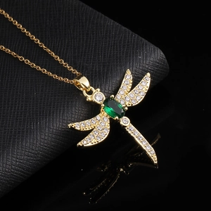 Macro shot of gold plated dragonfly pendant with green stone and pavé crystal details