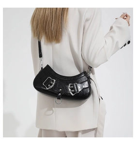 Detail of black glossy leather crescent bag featuring a metallic buckle and ring decoration