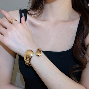 Polished gold-tone open cuff bracelet and ring set worn by a model in a close-up shot