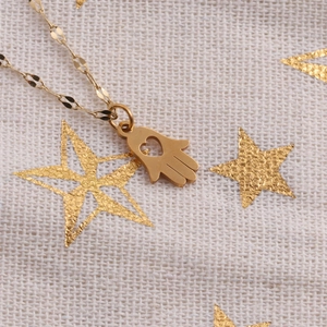 Close-up of golden Hamsa hand pendant with heart cutout and flat link chain on white fabric
