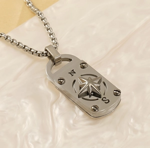 Détail macro du collier pendentif boussole argenté avec lettres gravées et motif étoile