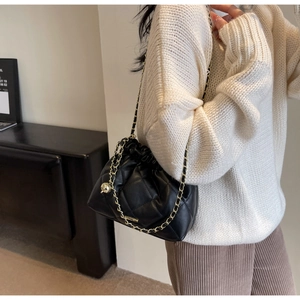 Close-up of black quilted bucket bag with gold chain strap worn by a model