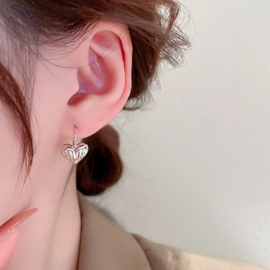 Close-up of silver textured heart earring showing detailed metal ridges on model