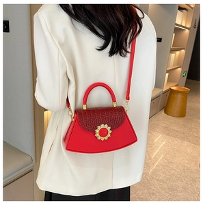 Detail der roten Handtasche mit Krokoprägung und goldener Sonne an einem Model