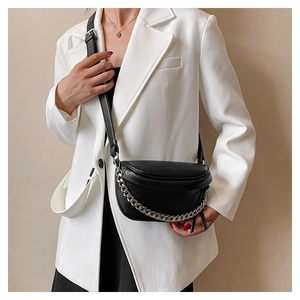 Close-up of black lychee-textured crossbody bag with chunky silver chain on white blazer