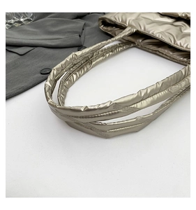 Detail of glossy gold puffer bag wide strap with premium stitching and padded texture