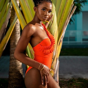 Detail of bright orange one-shoulder swimsuit featuring elegant ruffle trim and textured fabric