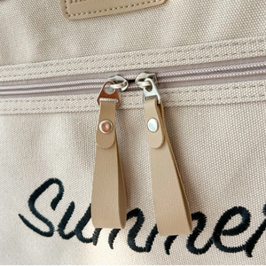 Detail shot of beige canvas tote with zipper closure and black Summer embroidery text