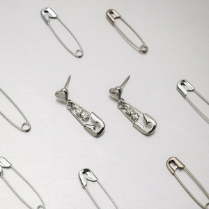 Silver safety pin earrings with crystal heart studs on a reflective metallic background