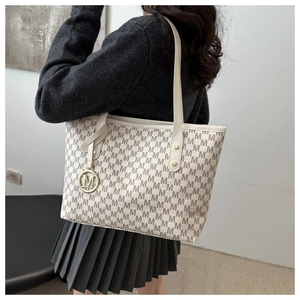 Detail of beige tote bag with brown pattern and golden M pendant charm on a shoulder strap