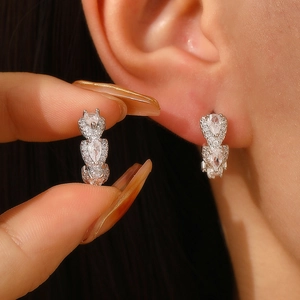 Close-up of silver earrings with three pear-shaped zircons worn on earlobe