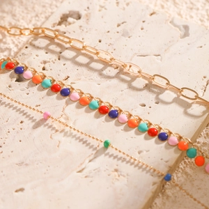 Close-up of golden necklaces with colorful enamel charms on a light stone surface