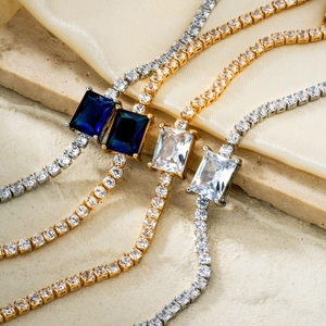 Elegant gold and silver tennis bracelets with square gemstones on a silk and stone background