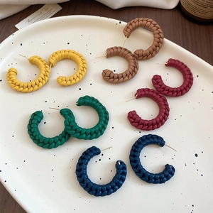 Detail of five multi-colored woven leather C-shaped hoop earrings on a ceramic tray