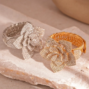 Floral crystal studded open cuff bracelet in gold and silver finish on stone background