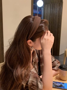 Close-up of a brown fabric headband and textured metal earrings in a warm indoor setting