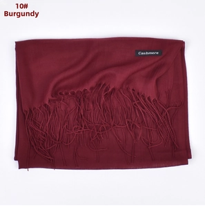 Detail shot of wine red cashmere-feel scarf featuring fringe edges and a woven label