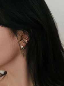 Detail shot of minimalist silver geometric crossover hoop earring and oval ear cuff on ear