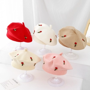 Detail of knitted baby beret hats in various colors with cherry embroidery patterns