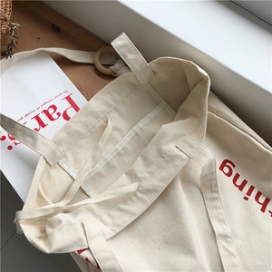 Close-up of beige canvas tote with red lettering and dual handles on a wooden surface