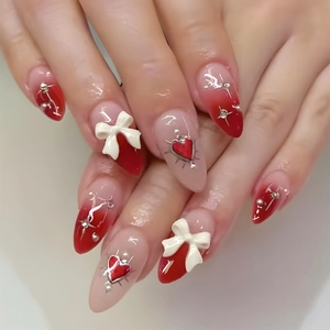 Detail of long almond press-on nails with 3D white bows and red heart charms