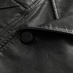 Close-up of black leather jacket lapel and button showing fine grain texture and stitching
