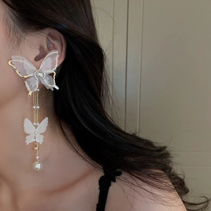 Close-up of white fabric butterfly earrings with gold tassels and pearls on model