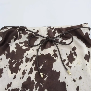 Détail macro du tissu satiné imprimé vache avec cordon marron et embouts dorés