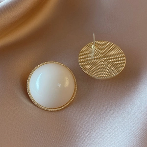 Macro view of cream white acrylic button earrings with gold trim and textured back