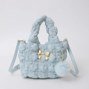 Détail d'un sac plissé en nylon bleu clair avec nœud doré et pompon en peluche assorti