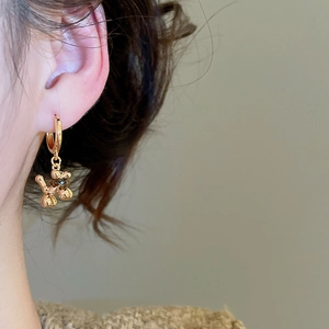 Detailed view of a gold-plated balloon dog earring with tiger eye stone on a model