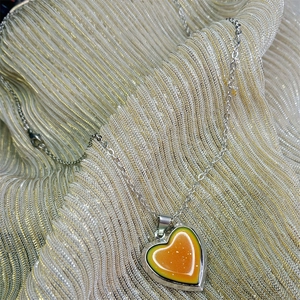 Detail of silver chain with a gradient color heart pendant on metallic fabric